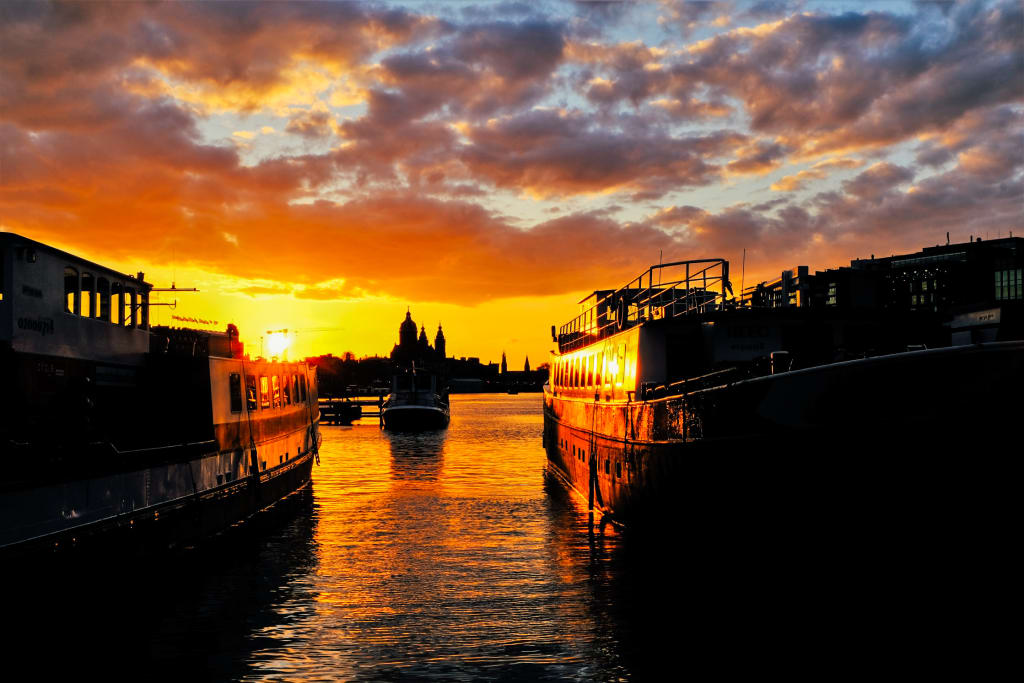 Tramonto su un canale olandese con barche e alberi riflessi nell'acqua, Paesi Bassi.